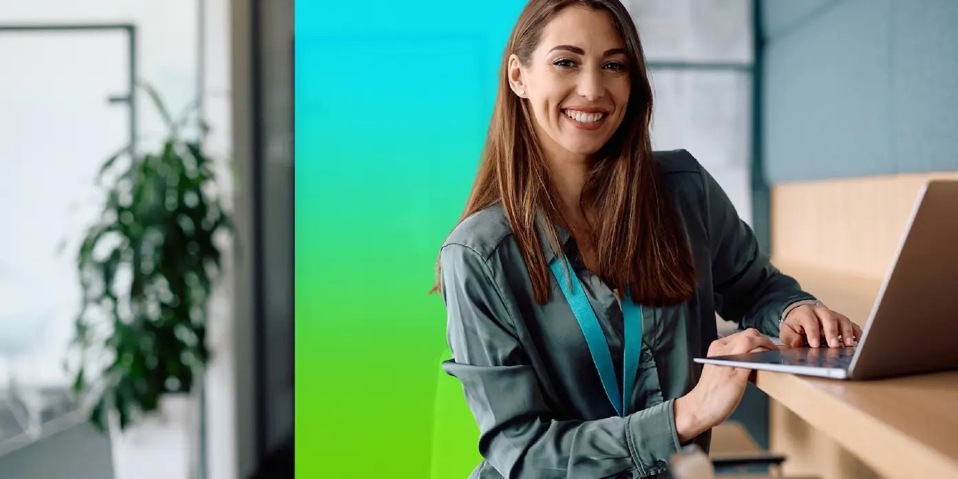 A woman in an office smiles while working on a laptop.