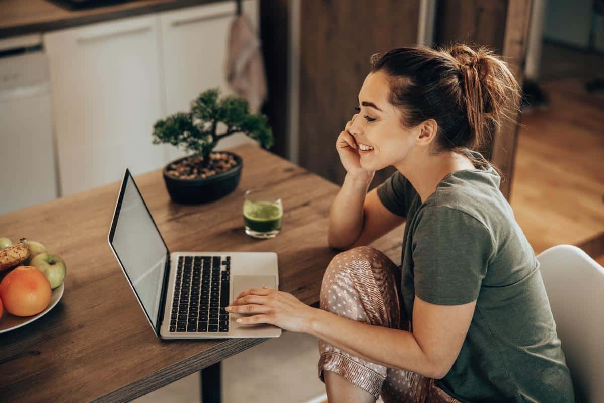 Woman Surfing The Net While Enjoying Breakfast In Her Kitchen At Home