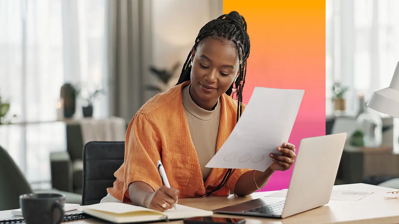 woman writing in a notebook while reviewing a report