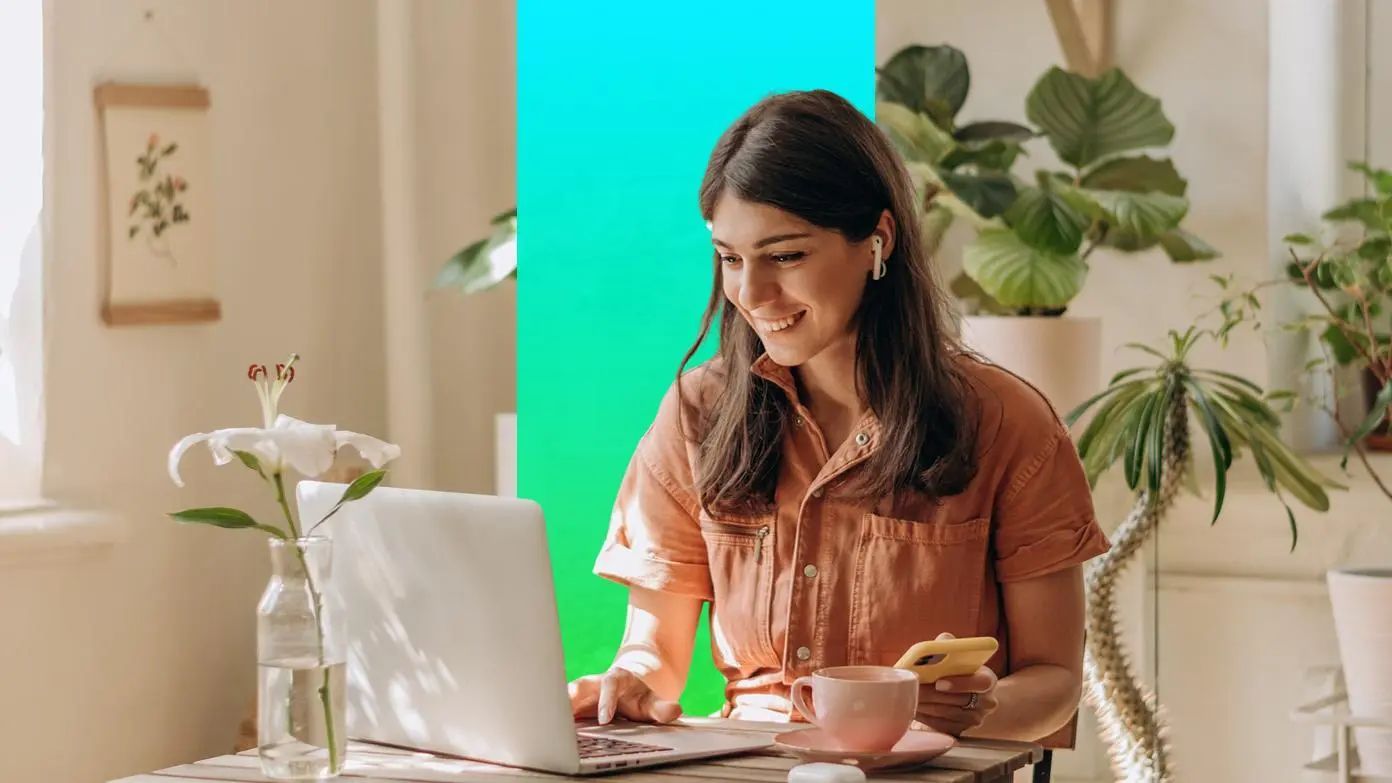 woman working on a laptop and also holding a cell phone