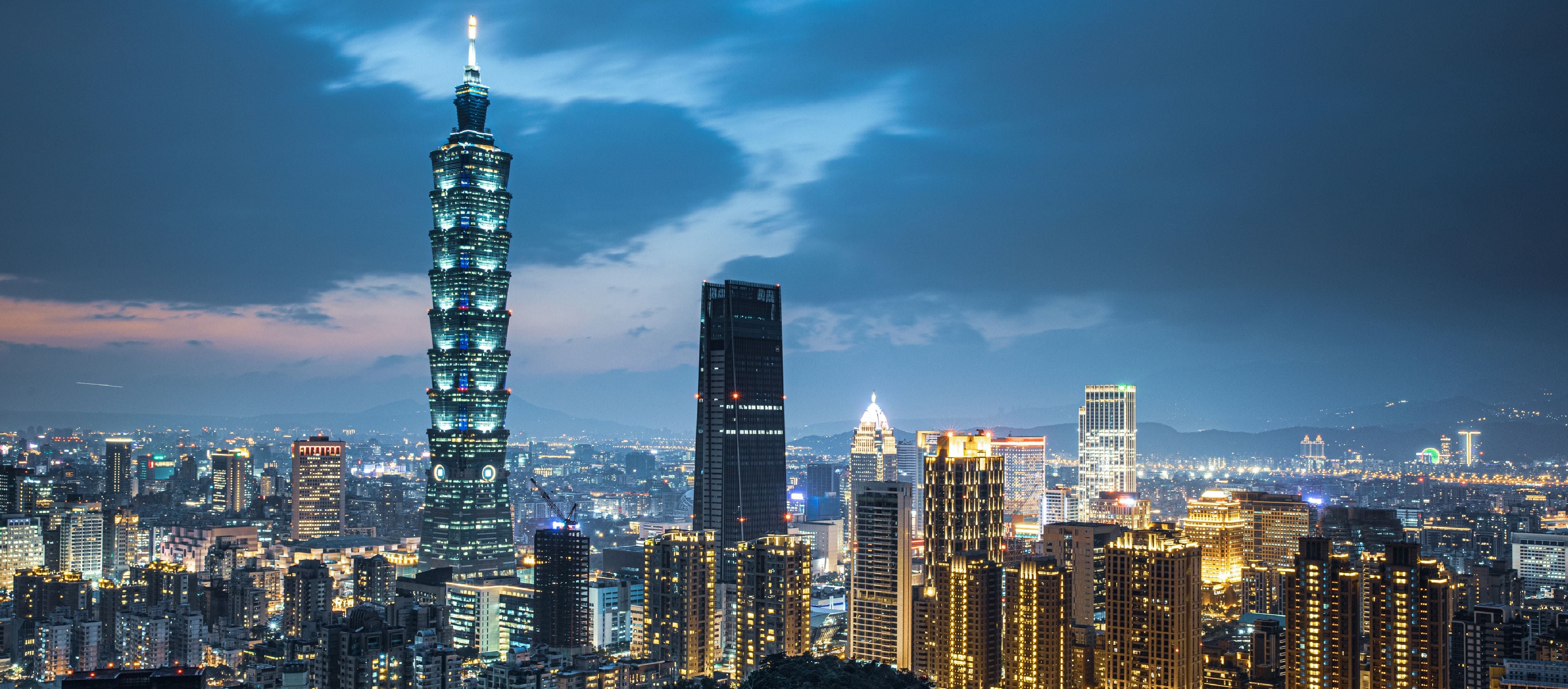 이 이미지는 황혼이나 새벽에 활기 넘치는 도시 경관을 보여주며, 꼭대기 중앙에 첨탑이 있는 눈에 잘 띄는 키가 크고 다층 건물이 지배합니다.