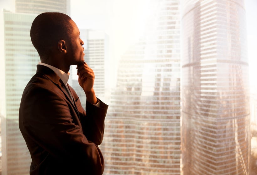 Young african-american thoughtful businessman looking through window on sunset city